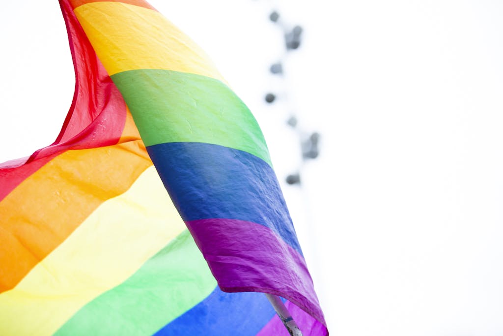 A colorful rainbow pride flag waves against a bright sky, symbolizing LGBTQ+ celebration and diversity.